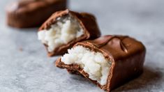 two pieces of chocolate covered with coconut on top of a gray countertop, one half eaten and the other half partially open