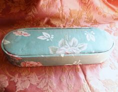 a blue and white case sitting on top of a pink flowered cloth covered bed