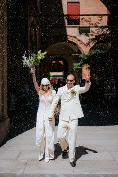 a man and woman dressed in white are walking through the rain with their hands in the air