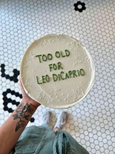 a person holding up a cake with the words too old for leo dicaprio on it