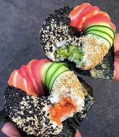 two sushi rolls are being held up by someone's hand with sesame seeds on them