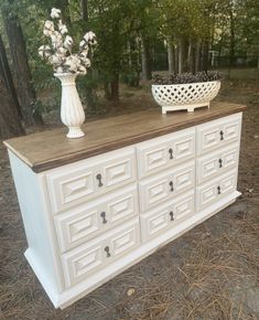 a white dresser sitting on top of a forest floor next to a potted plant