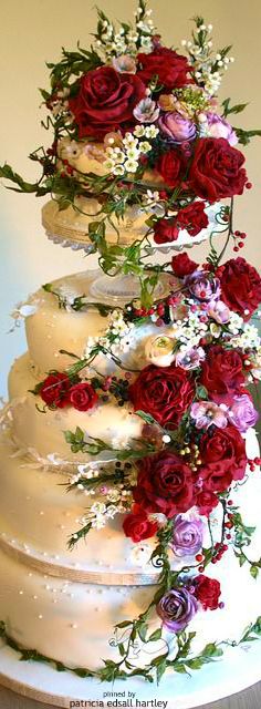 a three tiered cake with red and purple flowers on the top is covered in white frosting