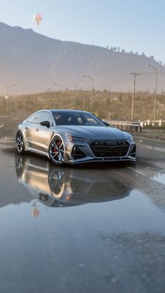 a silver sports car is parked on the side of the road in front of a mountain