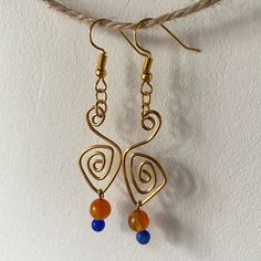 two pairs of earrings hanging from a rope on a wall, one with orange beads and the other with blue beads