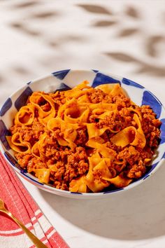 a blue and white bowl filled with pasta on top of a table next to a fork