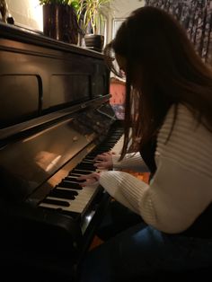 a woman is playing the piano in her living room at night time, with long hair flowing over her face