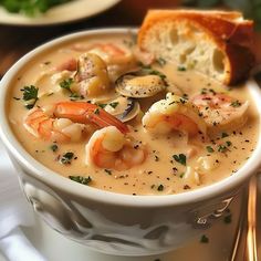 a bowl of soup with shrimp, clams and bread