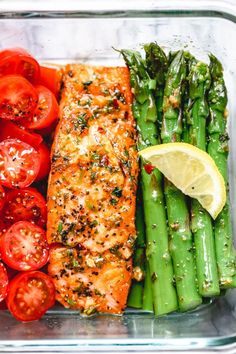 salmon, asparagus and tomatoes in a glass dish with lemon wedges on the side