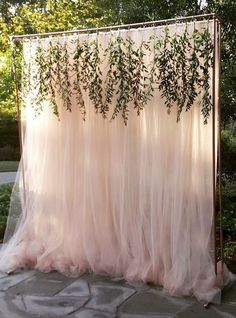 an outdoor wedding ceremony with pink tulle and greenery draped over the altar area