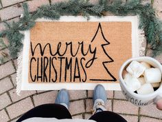 someone is holding a coffee cup in front of a door mat with merry christmas written on it