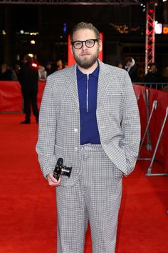 a man in a suit and tie standing on a red carpet with his hands in his pockets