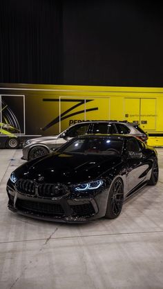 two black cars parked next to each other in front of a yellow wall and floor