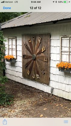 a wooden clock mounted to the side of a white building with flowers in front of it