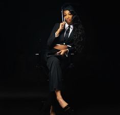 a woman in a suit and tie sitting on a chair holding an umbrella over her head