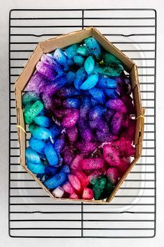 a box filled with different colored rocks on top of a wire rack next to a white wall