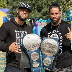 two men standing next to each other holding up their wrestling belts and giving the thumbs up