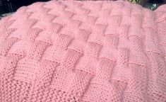 a pink knitted blanket sitting on top of a bed
