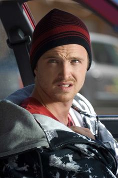 a man sitting in the back seat of a car wearing a beanie and looking at the camera