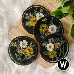 four black plates with yellow and white flowers on them sitting on a furnishing