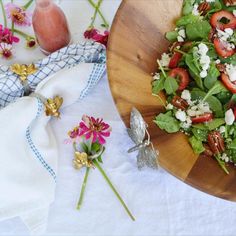 a salad with strawberries and goat cheese is on a wooden plate next to flowers