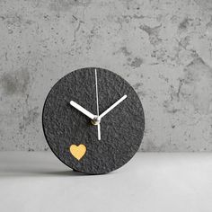 a clock with a heart on the face is shown in front of a concrete wall