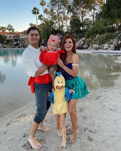 three people standing on the beach with one holding a baby and wearing a costume that looks like a fish