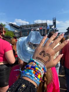 a person with their hand up in the air at a music festival, wearing bracelets and a cowboy hat