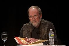 an older man sitting at a table with a book in front of him and a glass of water