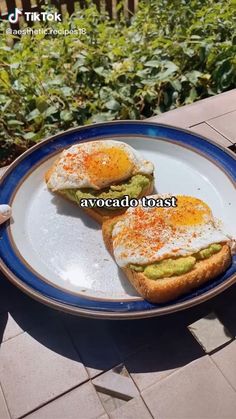 someone is holding a plate with two toasts on it that have eggs and avocado in them
