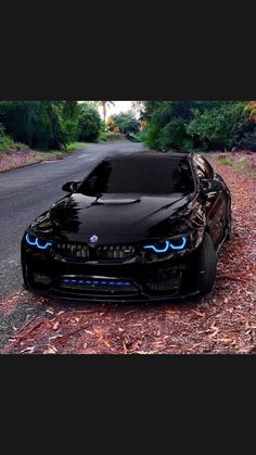 a black car parked on the side of a road next to some bushes and trees