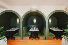 the interior of a restaurant with green velvet booths and wooden floors, potted plants on either side of the tables