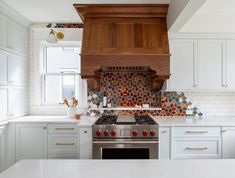 a kitchen with an oven, stove and counter tops in white cabinets that are decorated with colorful tiles