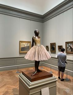 a person standing next to a statue in a room with paintings on the walls and wooden floors