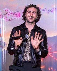 a man in a black leather jacket is holding his hands up to the air and smiling