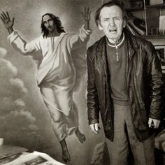 a black and white photo of a man standing in front of a painting of jesus