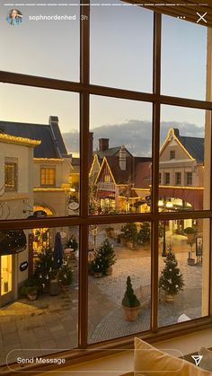 the view from an open window looking out onto a town square at christmas trees and buildings