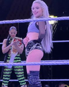 two women standing next to each other on top of a wrestling ring with one holding a belt