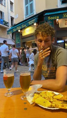 a man sitting at a table with two glasses of beer and food in front of him