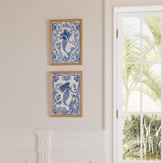 two blue and white tiles are hanging on the wall next to a window with palm trees in the background