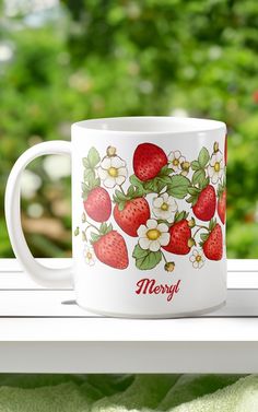 a white coffee mug with strawberries and flowers on it sitting on a window sill