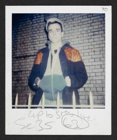 an old photo of a man standing in front of a brick wall with writing on it