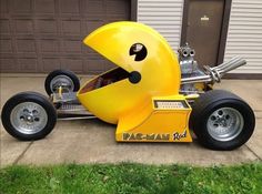 a yellow race car is parked in front of a garage with two large tires on it