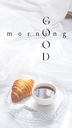 a cup of coffee next to a croissant on a plate with the words good morning d