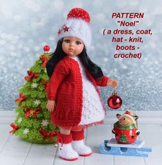 a doll is standing next to a small christmas tree with a red and white knitted hat