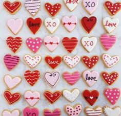 cookies decorated with different types of hearts on a white counter top, one cookie has the word love written in large letters and is surrounded by smaller heart shapes