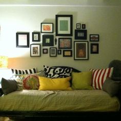 a day bed with lots of pillows and pictures on the wall above it in a living room