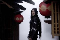 a woman with long black hair standing in front of red and white lanterns on the street