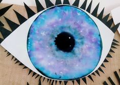 an eye with blue and purple paint on it's iris is surrounded by black spikes