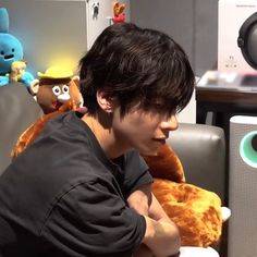 a young man sitting in front of a computer with stuffed animals on the wall behind him